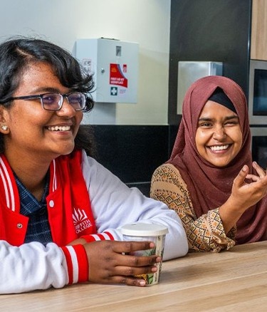 Three young adults chat at a kitchen counter with a fruit bowl in front of them.
