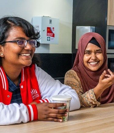 Three young adults chat at a kitchen counter with a fruit bowl in front of them.