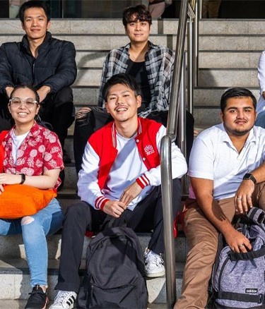 Group of diverse students sitting on stairs, smiling at the camera.