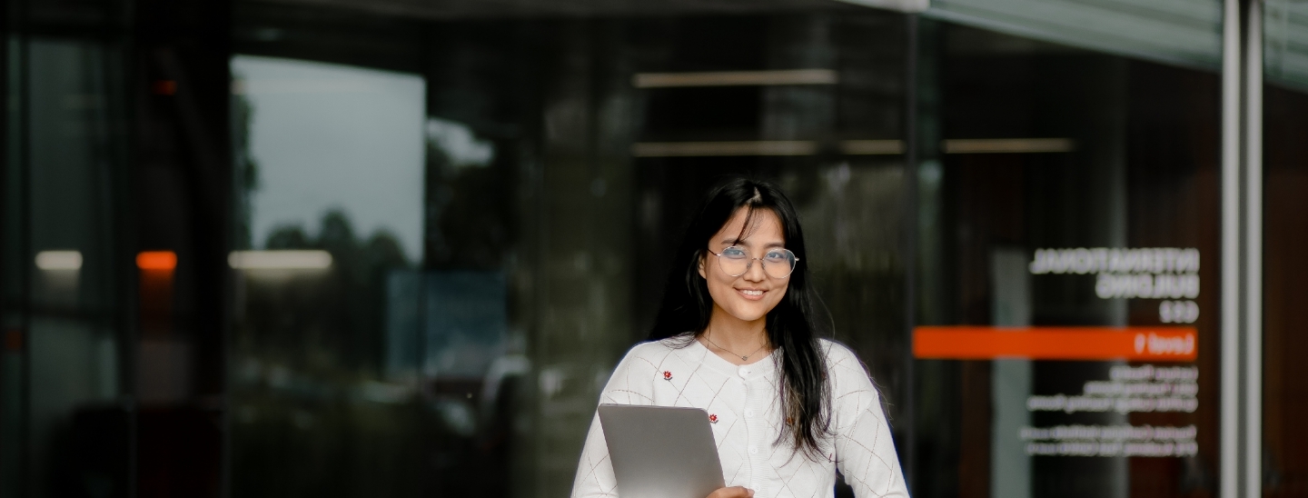 Student outside building holding laptop