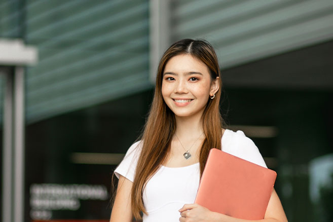 Student outside smiling holding documents