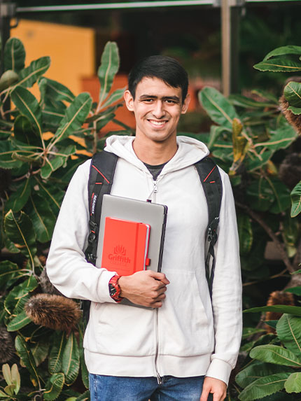 Student outside trees holding book