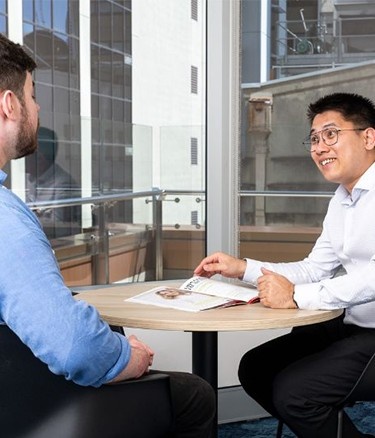 Two men have a discussion at a small table in a modern office.
