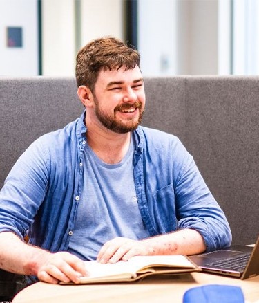 Two people talking in a study booth with a laptop and book.