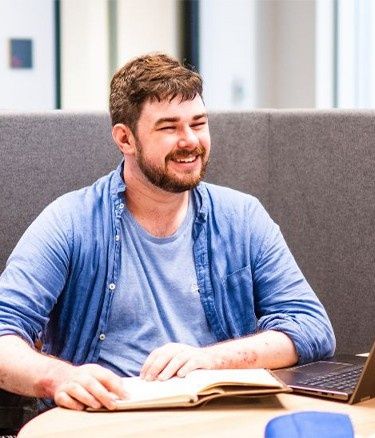 Two people talking in a study booth with a laptop and book.
